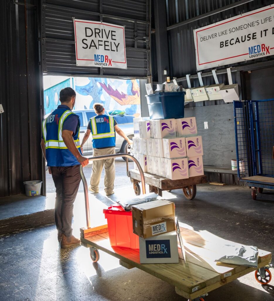 MedRx Logistics Team Members Roll Carts from the Warehouse to Delivery Vehicles